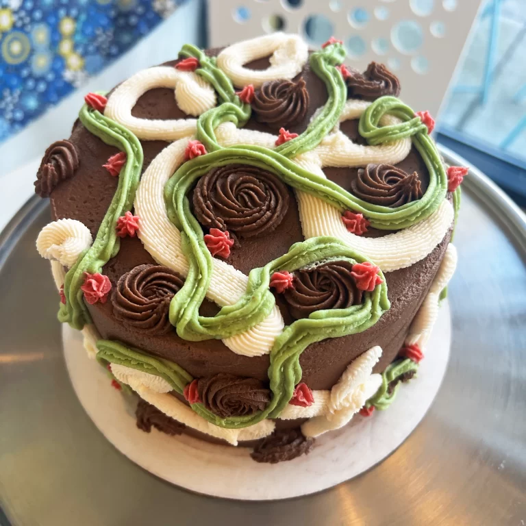 Chocolate cake with intricate green, white, and red frosting swirls and roses.